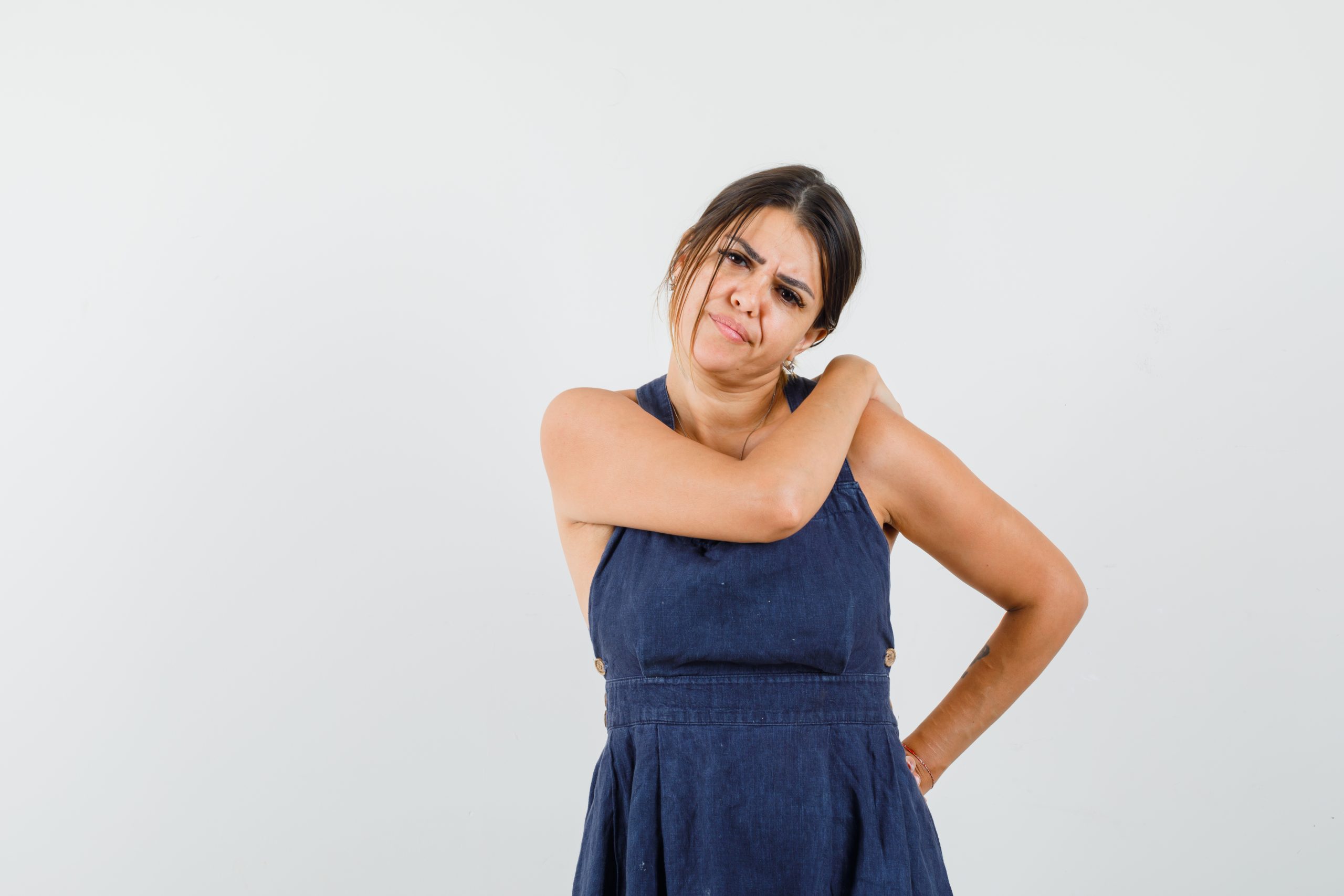 Young woman suffering from shoulder pain in dress and looking uncomfortable , front view.